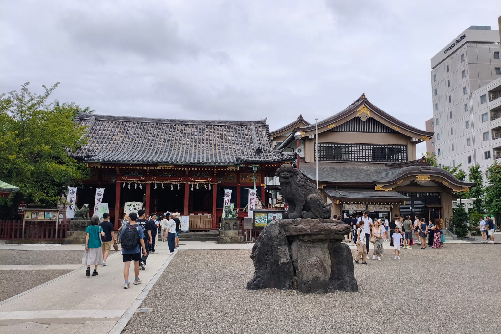 A shrine building with a dark tiled roof in the temple grounds at Asakusa, visitors crossing the square
