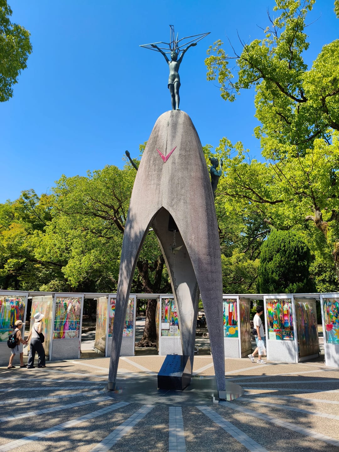 The Children’s Peace Monument, a tall curved arch topped by a bronze figure holding a paper crane, with cases of folded cranes behind
