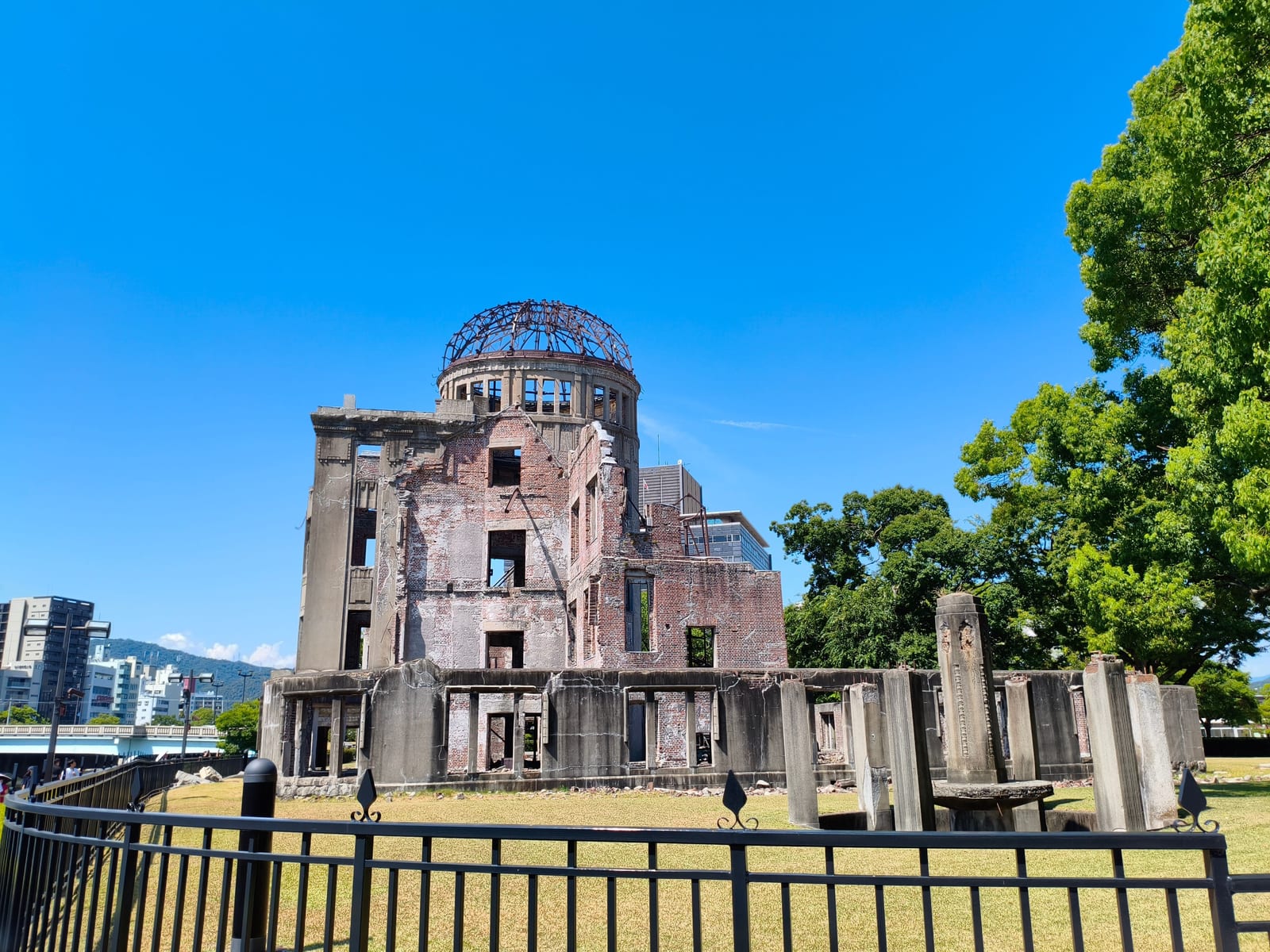 The ruined shell and exposed dome framework of the Atomic Bomb Dome, standing behind railings with trees around it