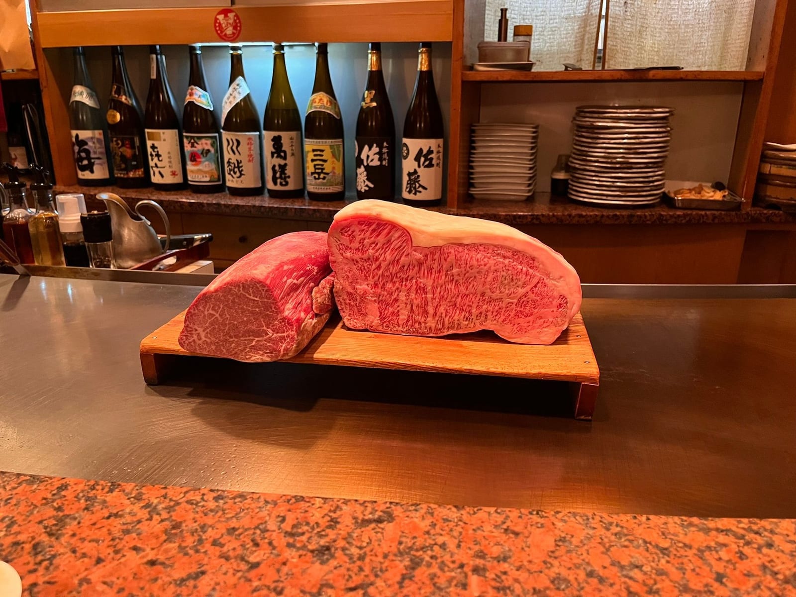 A cut of raw marbled A5 wagyu beef presented on a wooden board at a restaurant counter, bottles on the shelf behind
