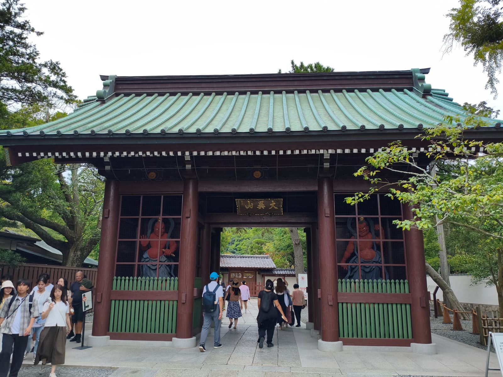 The green-roofed entrance gate at Kotoku-in with visitors walking through