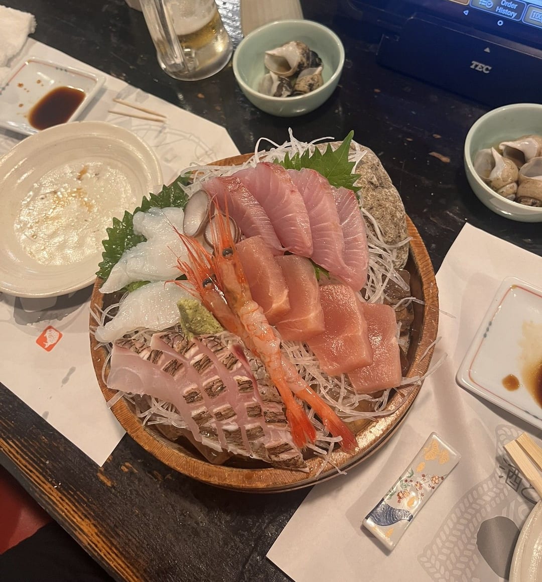 A sashimi platter of salmon, sweet shrimp and white fish on shredded radish in a wooden bowl