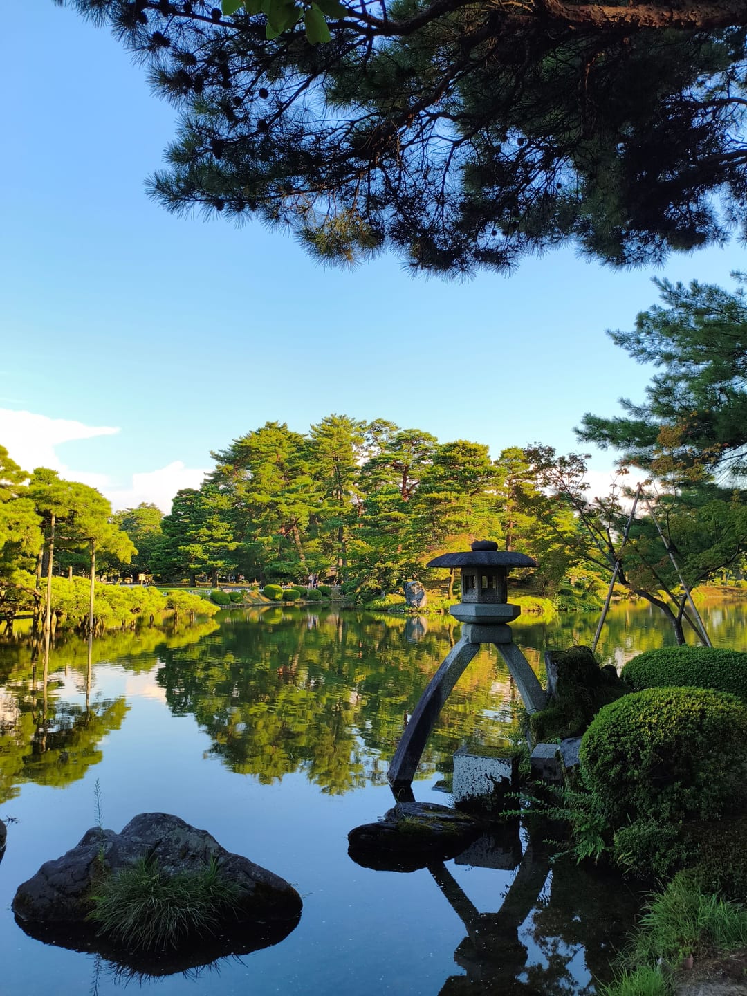 The two-legged Kotoji-toro stone lantern standing at the edge of a still pond, trees reflected in the water