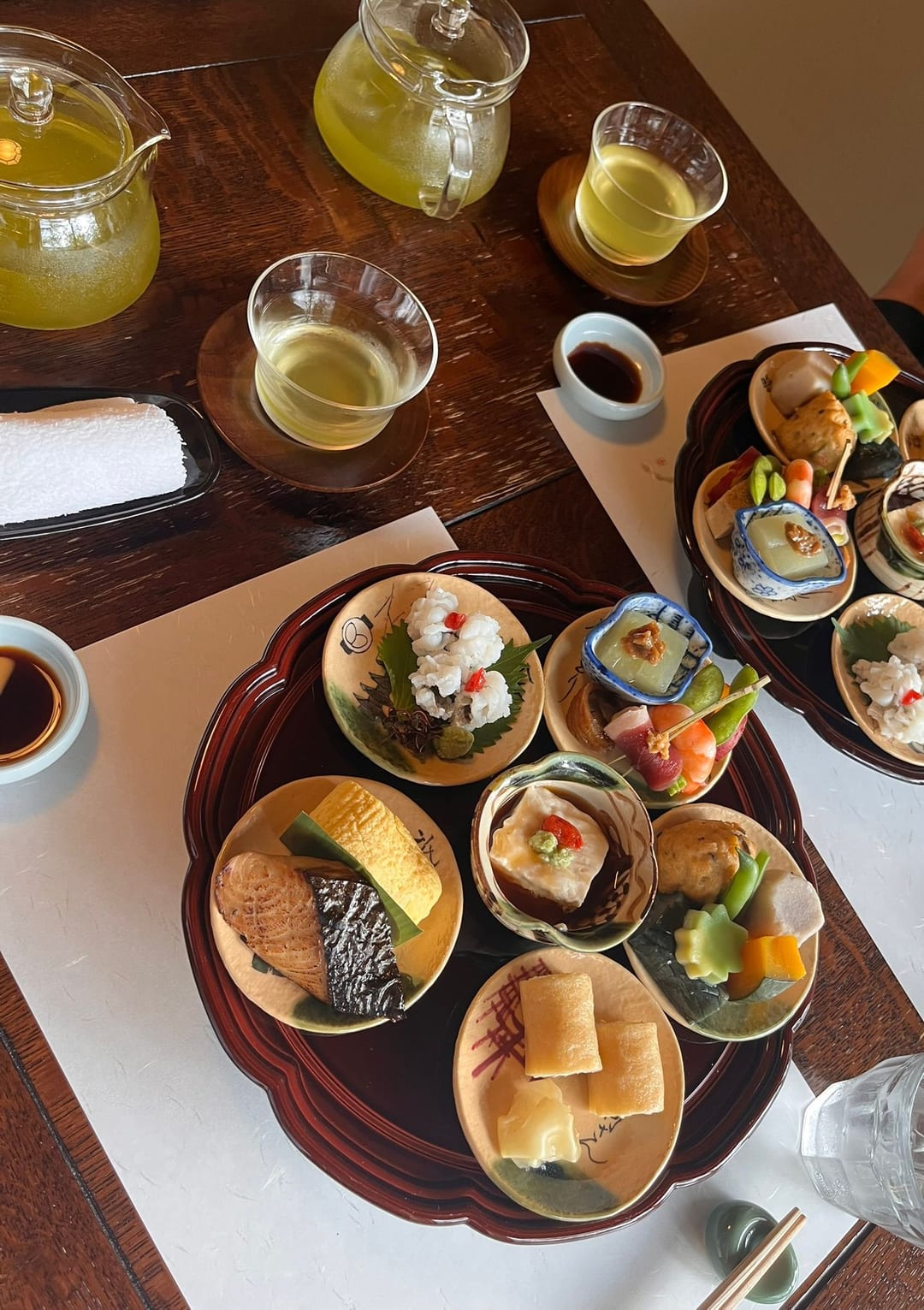 A Kyoto-style bento of many small dishes arranged on a lacquer tray, with pots of green tea beside it