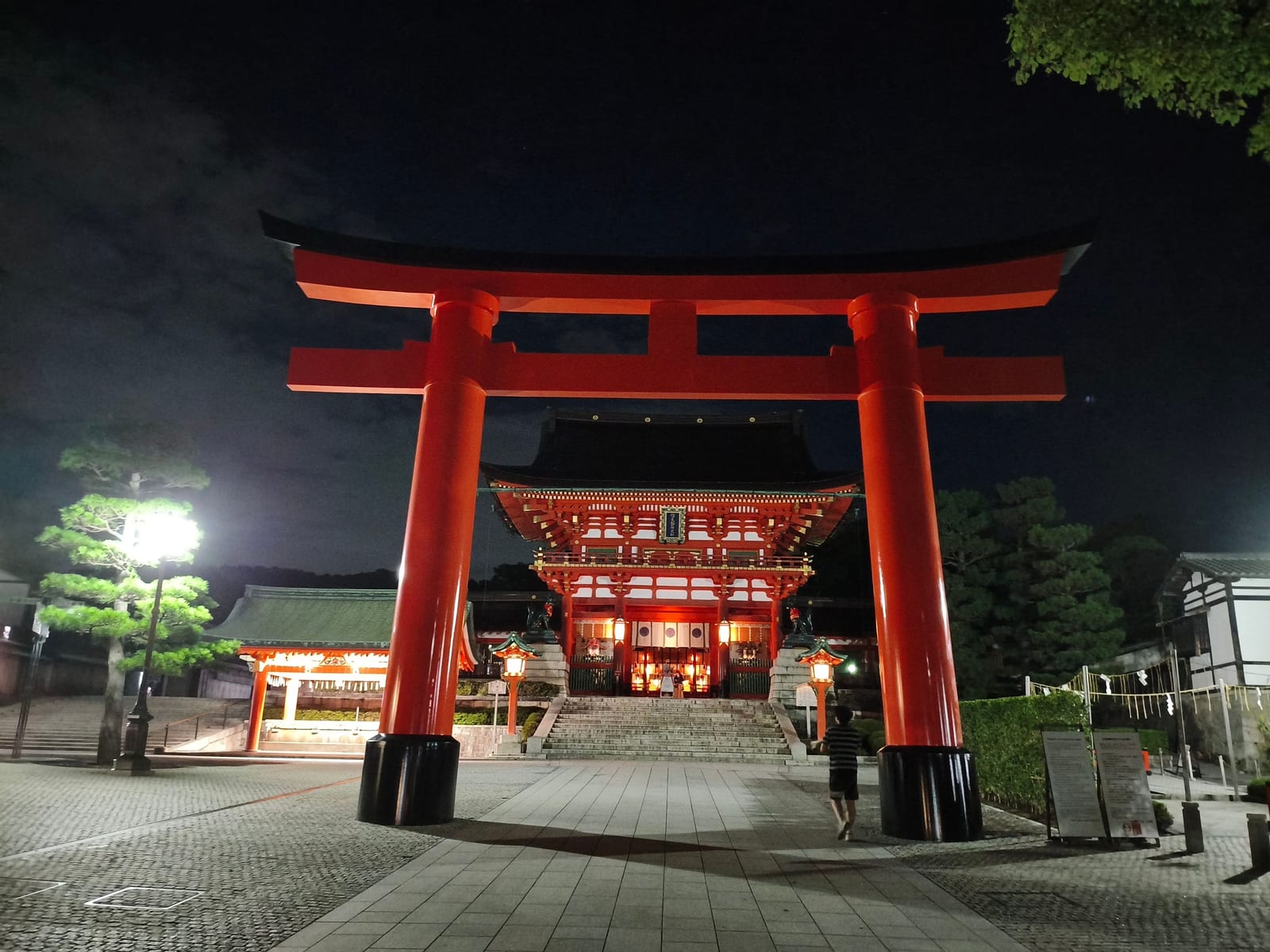 The great vermilion torii and the lit Romon gate at Fushimi Inari at night, with nobody in the square