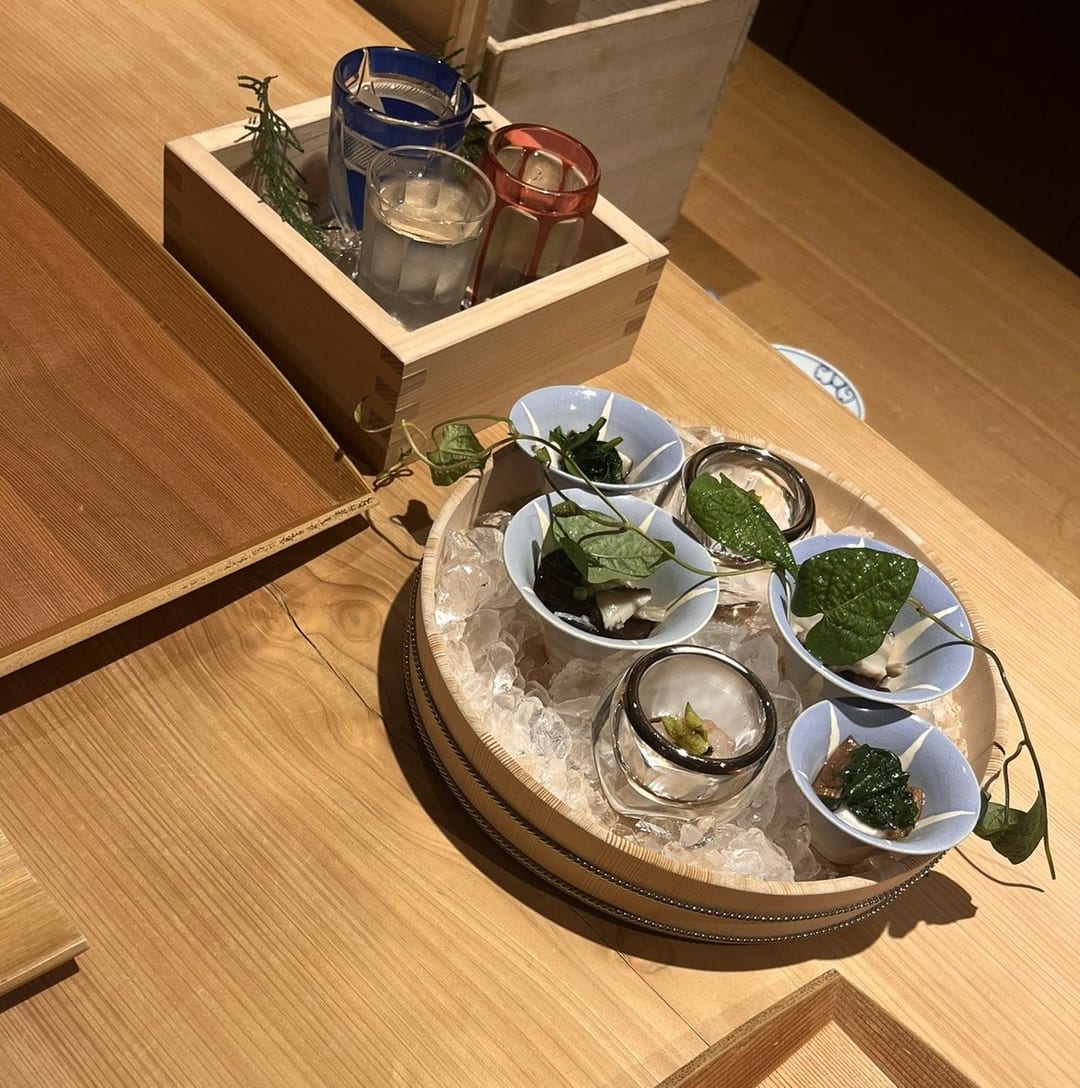 Small bowls set on crushed ice in a round tray, beside a wooden box holding three cut-glass sake cups