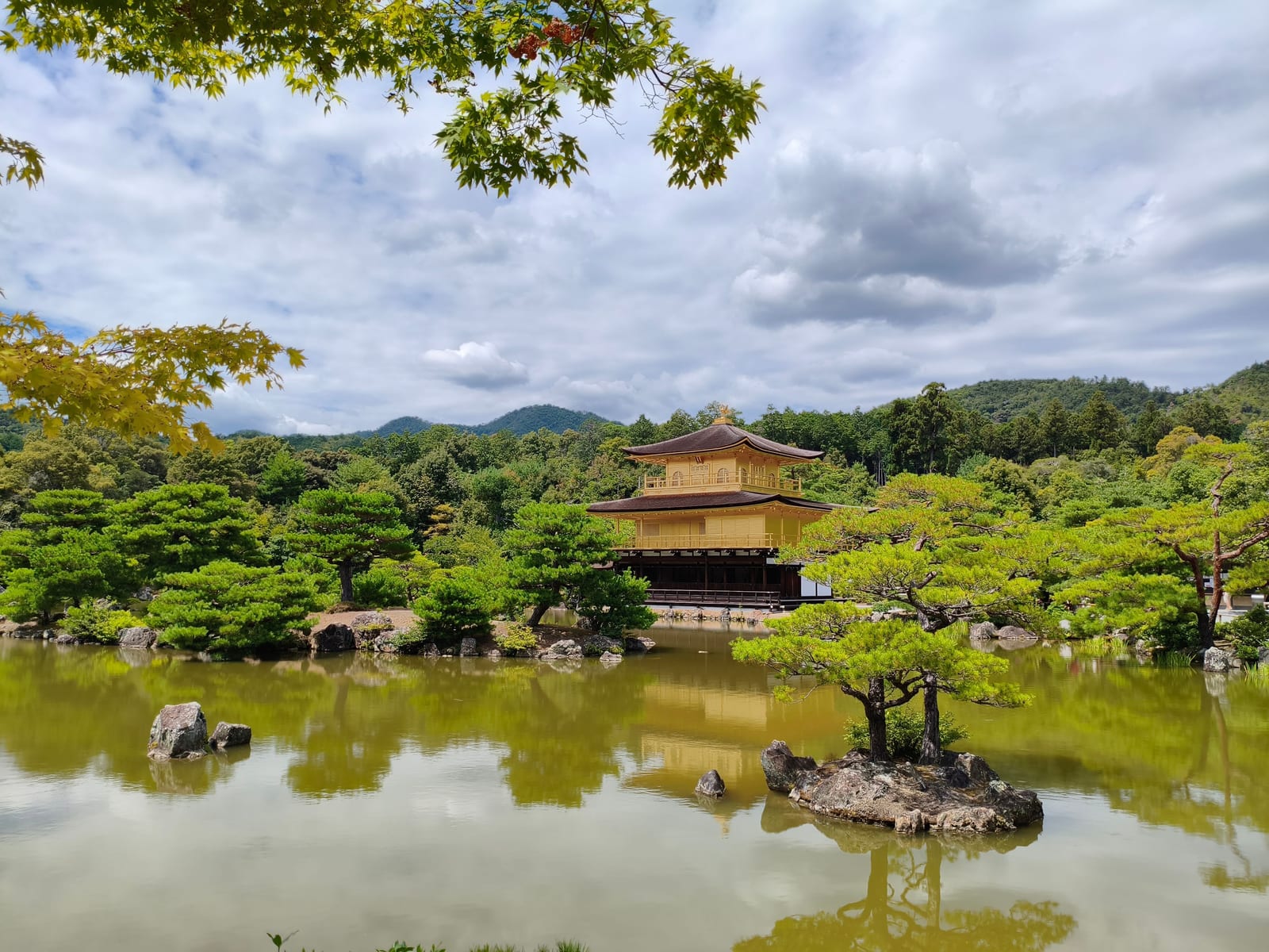 The gold-leafed Kinkaku-ji pavilion reflected in the pond, framed by maple leaves