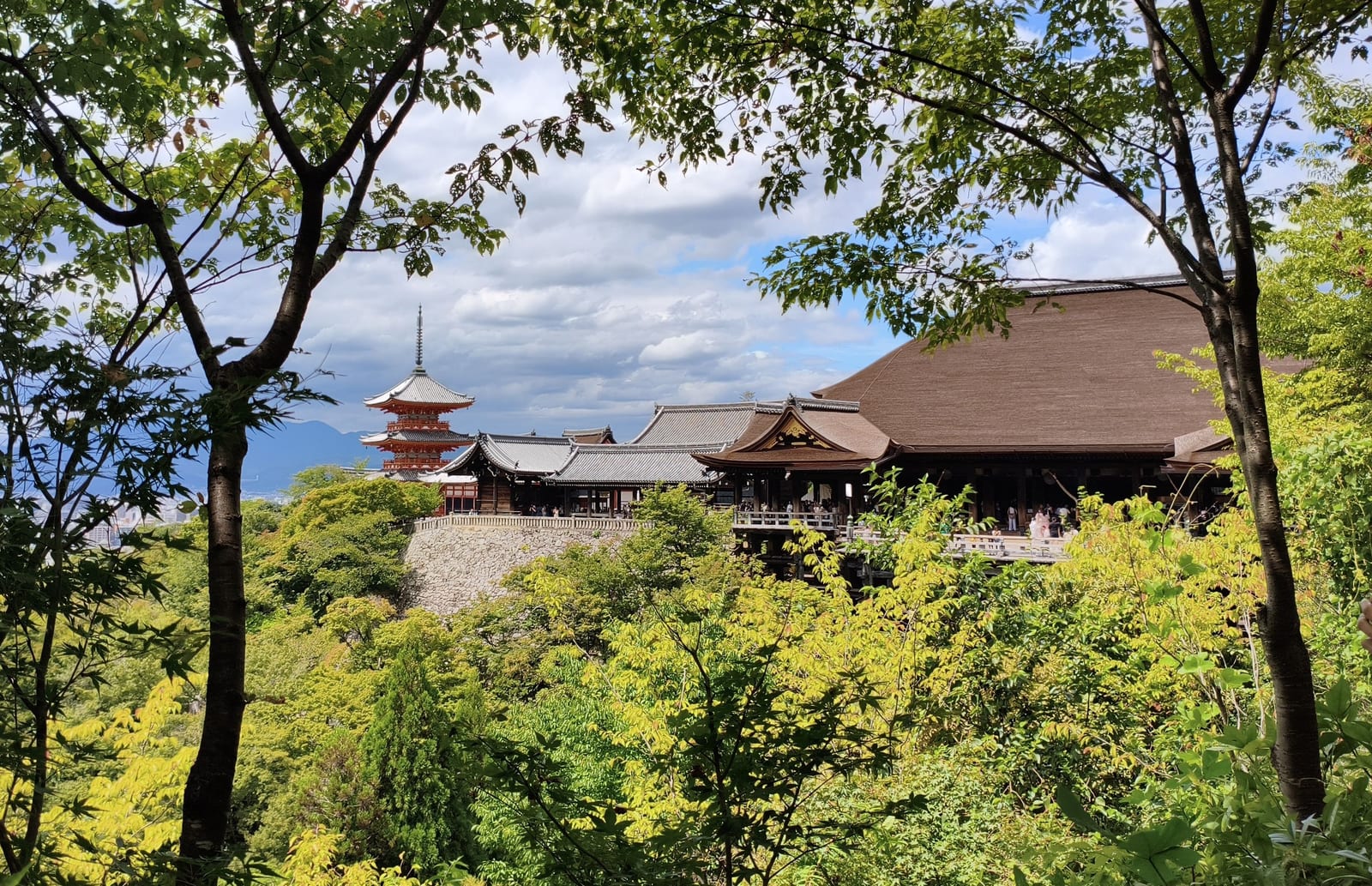 The wooden main hall of Kiyomizu-dera on the hillside, with its three-storied pagoda behind, framed by trees