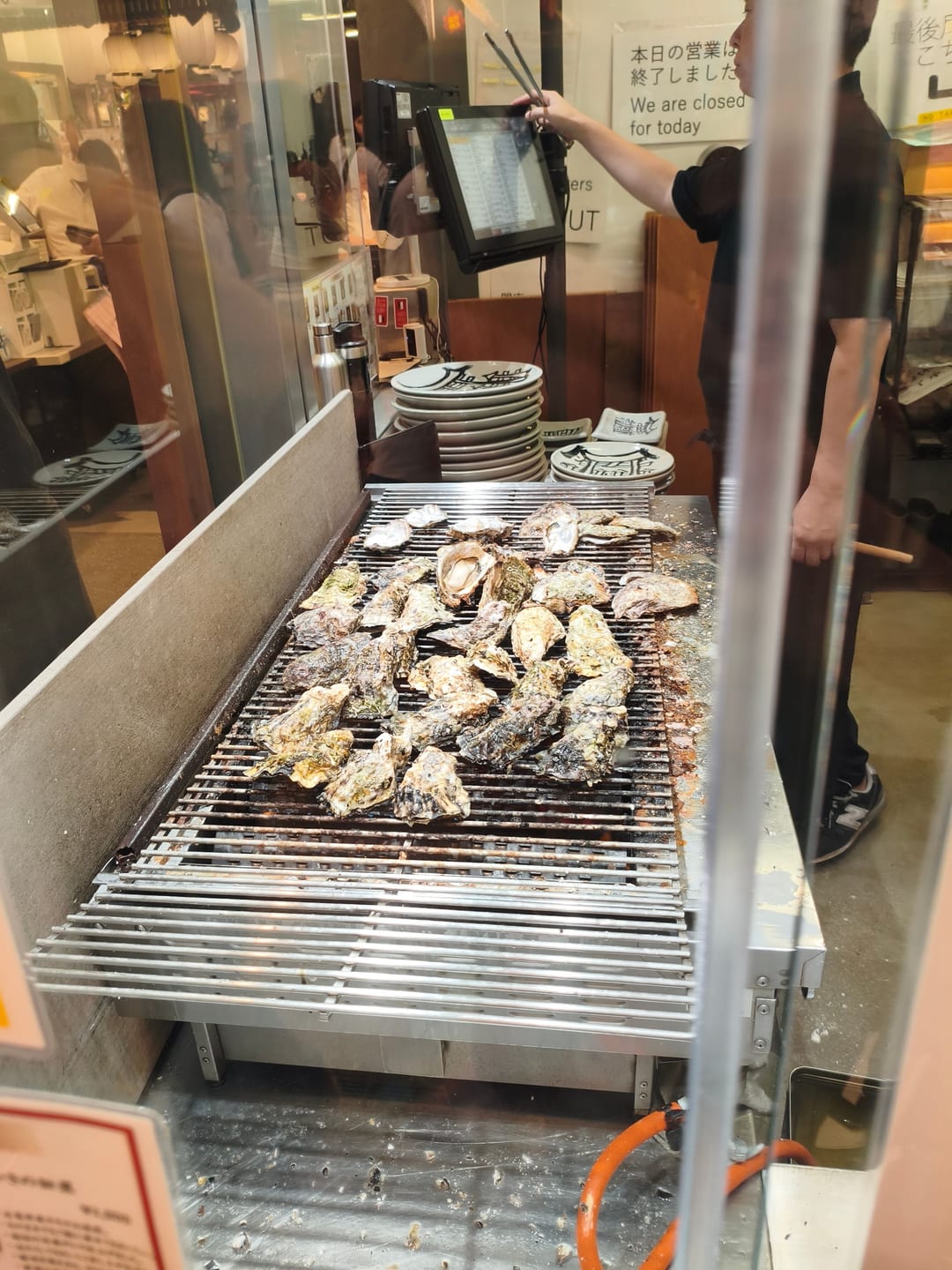 Oysters in their shells cooking on a grill at the open front of a restaurant