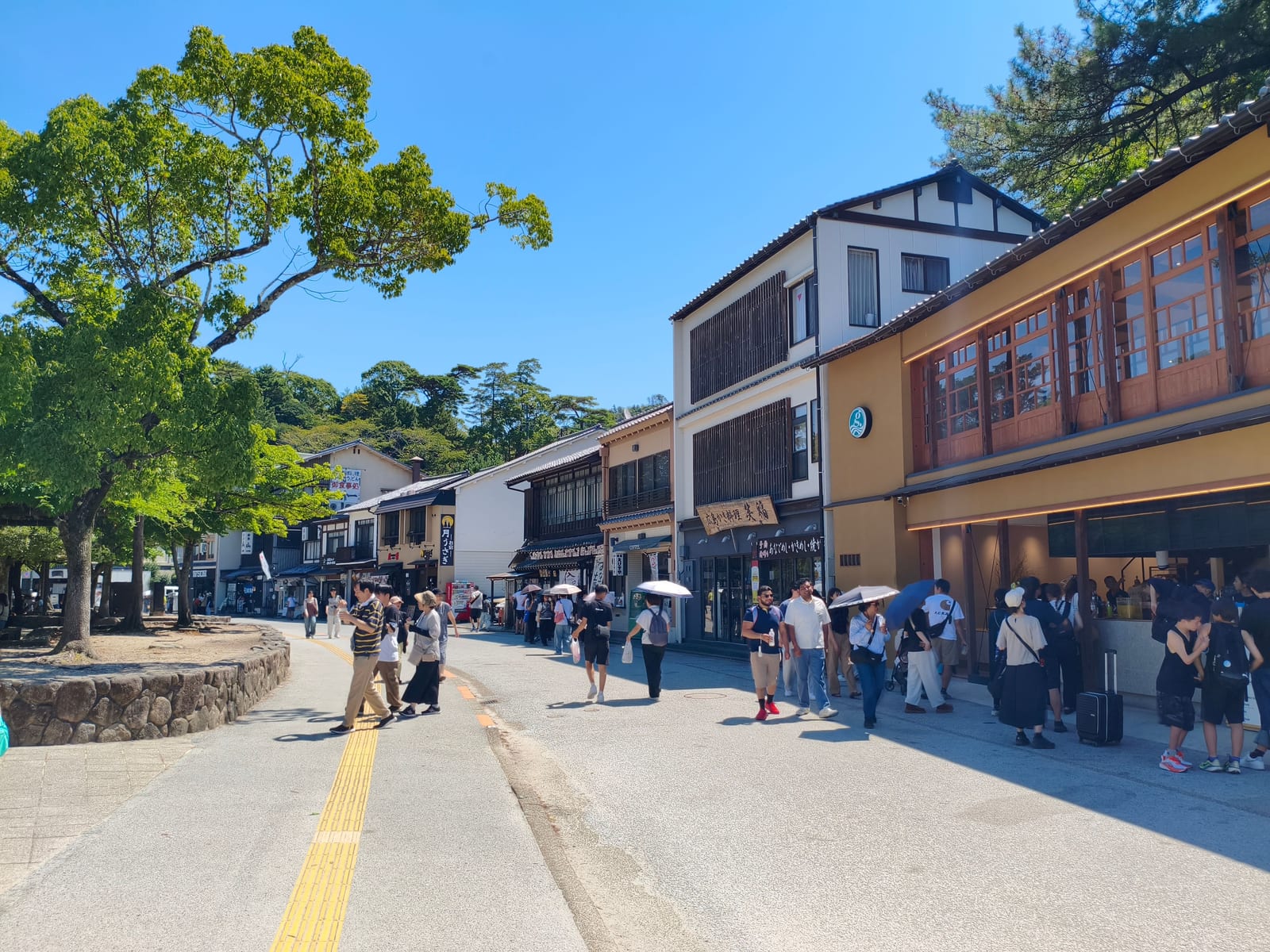 A busy shopping street on Miyajima lined with wooden shopfronts, crowds walking along it