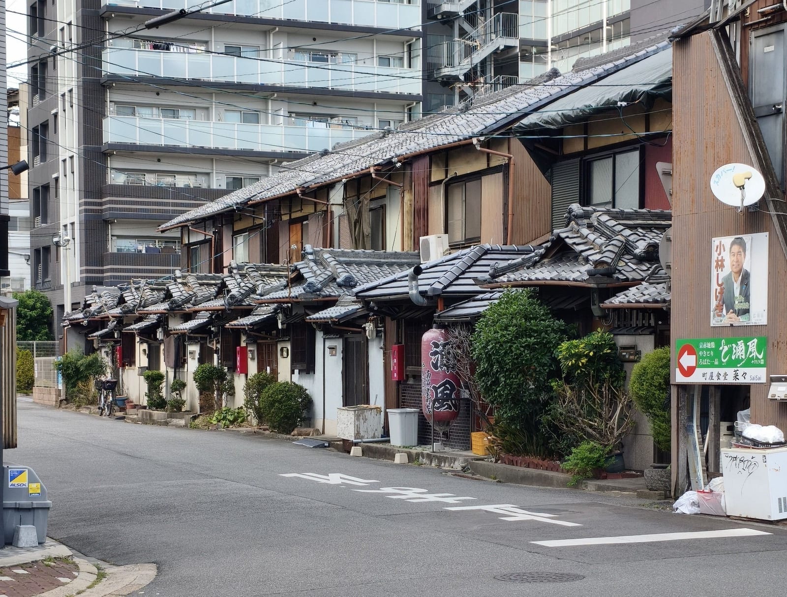 A row of low wooden Edo-period townhouses with tiled roofs in Naramachi, a modern apartment block rising behind them