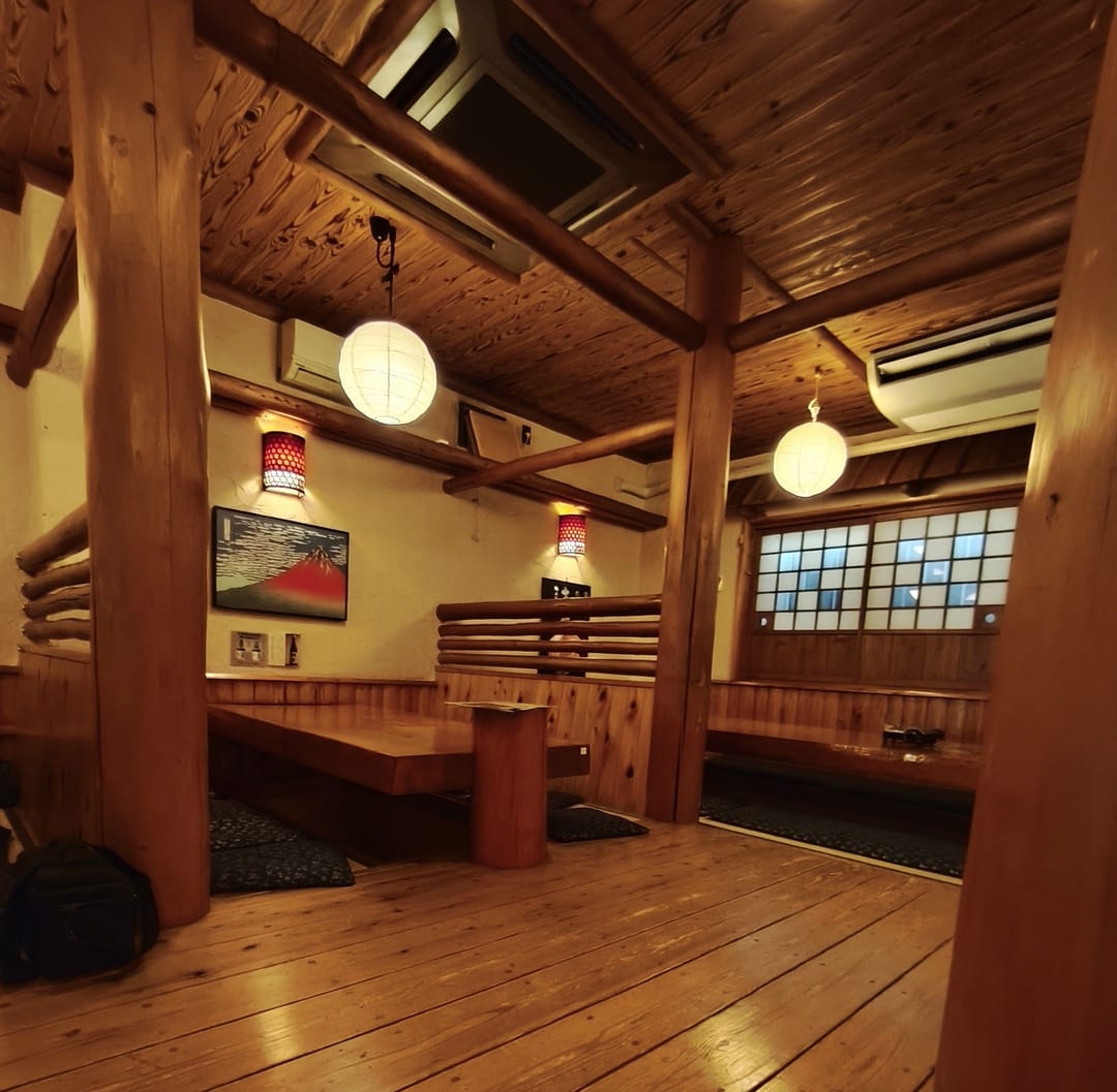 The dining room of a Japanese restaurant with low wooden tables, paper lanterns and sunken floor wells for your legs