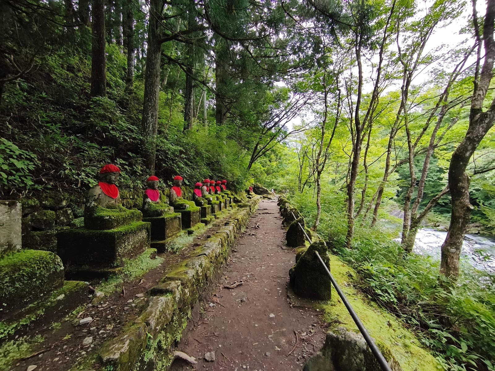 A forest path lined with moss-covered stone Jizo statues in red bibs, the Daiya River rushing past on the right