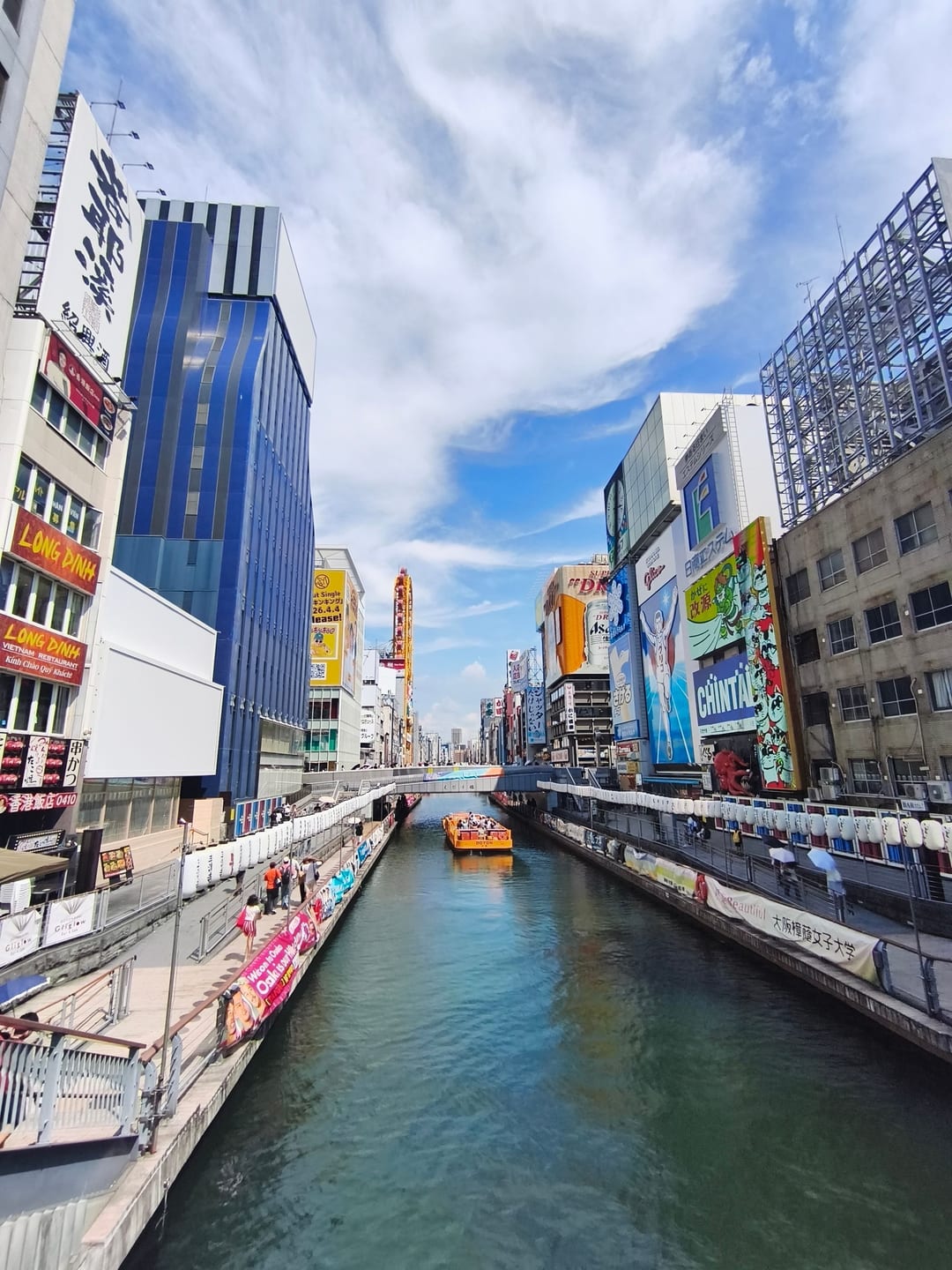 The Dotonbori canal lined with tall billboards on both banks, a tour boat coming down the middle