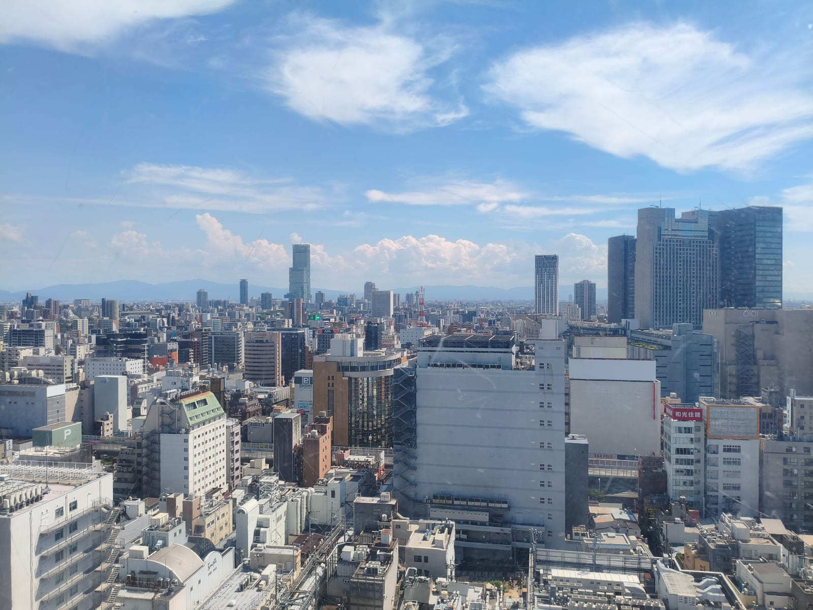 The rooftops of Osaka seen from high up, towers on the skyline under a blue sky