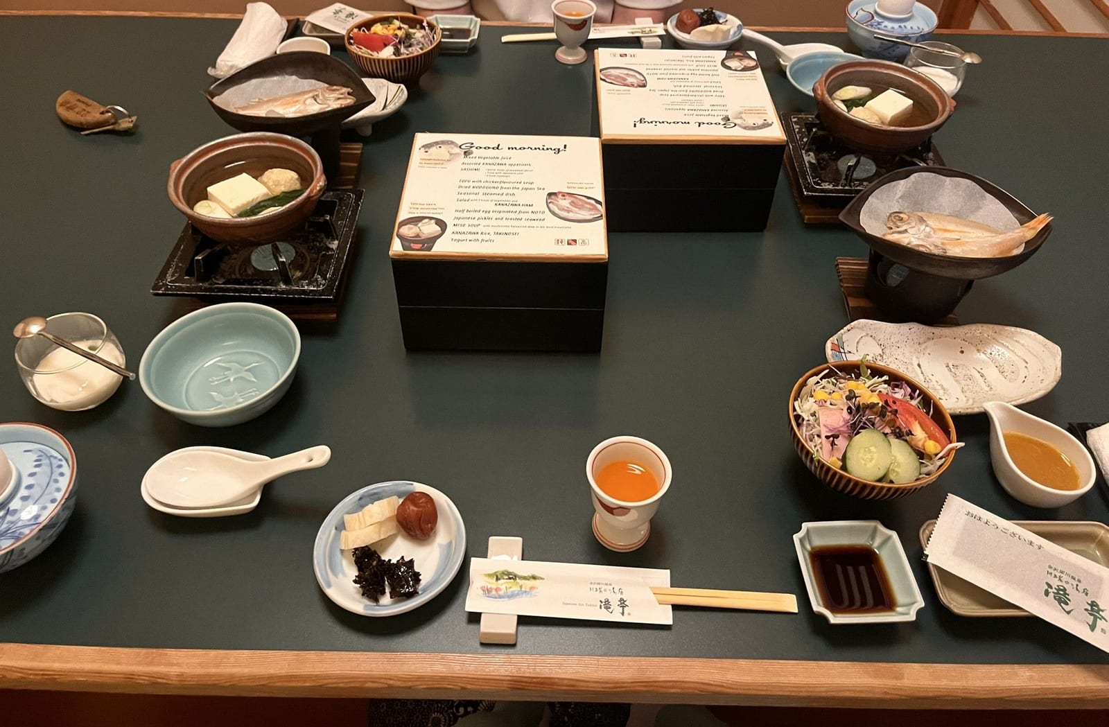 A Japanese breakfast spread across a table in many small dishes, with lidded pots and a teapot
