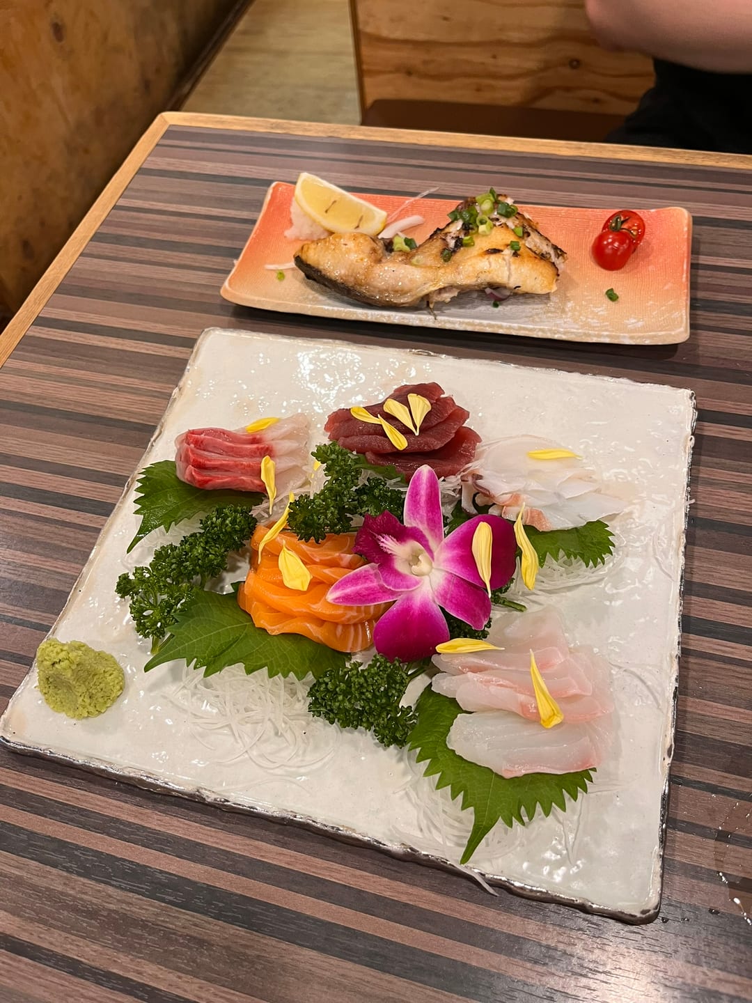 A sashimi platter with grilled fish, garnished with an orchid