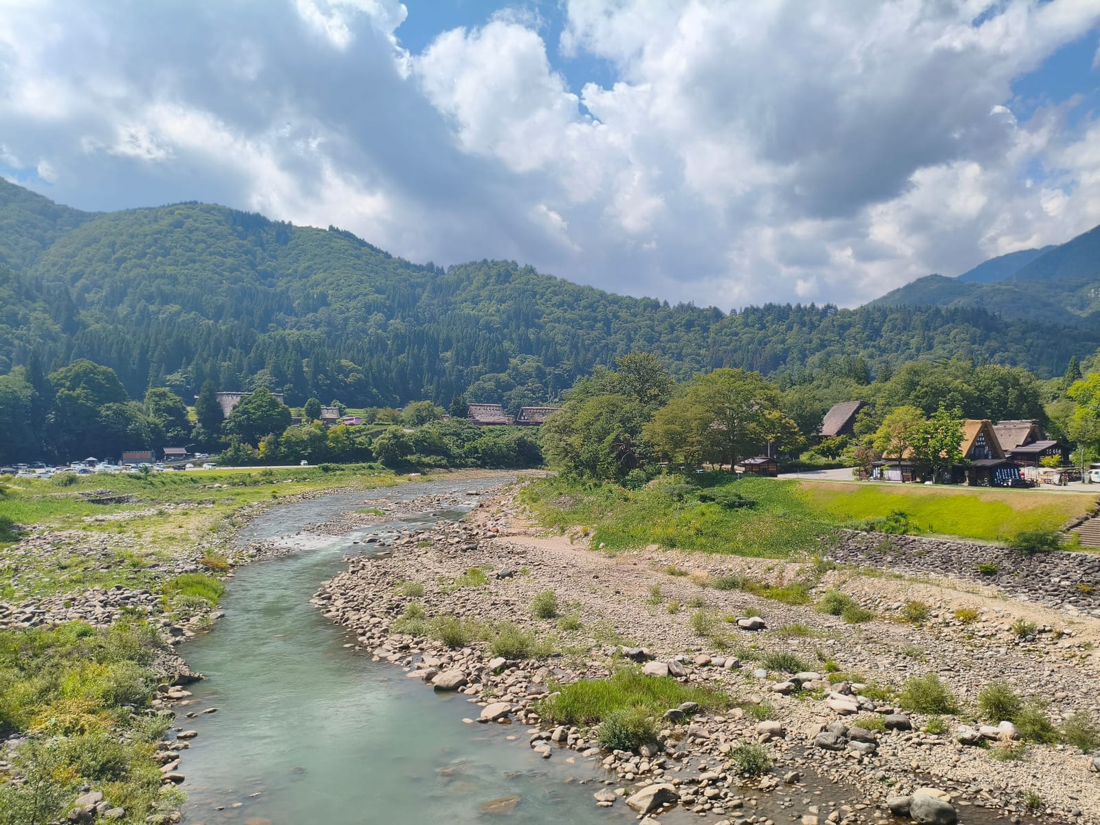 A clear mountain river running over stones past the village, forested hills rising behind