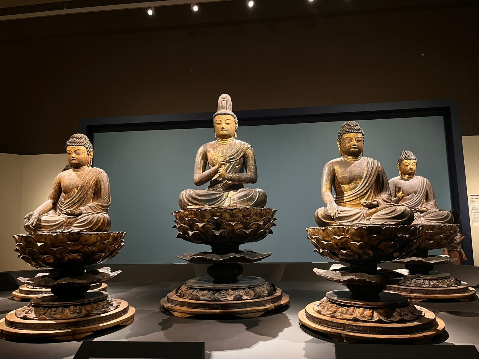 Four gilded seated Buddha statues on lotus pedestals in a dimly lit gallery
