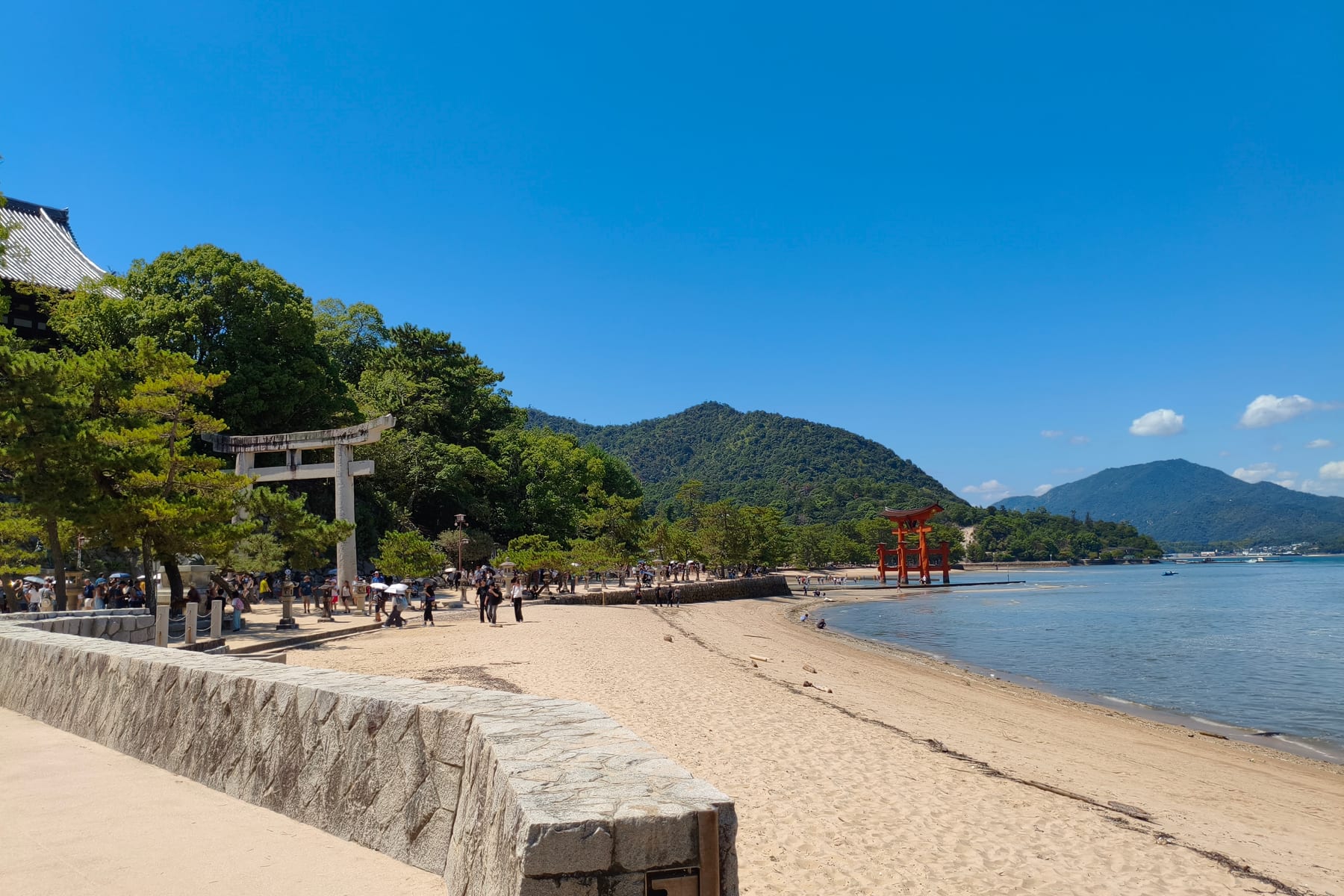 The beach on Miyajima with the red floating torii out on the water and mountains behind