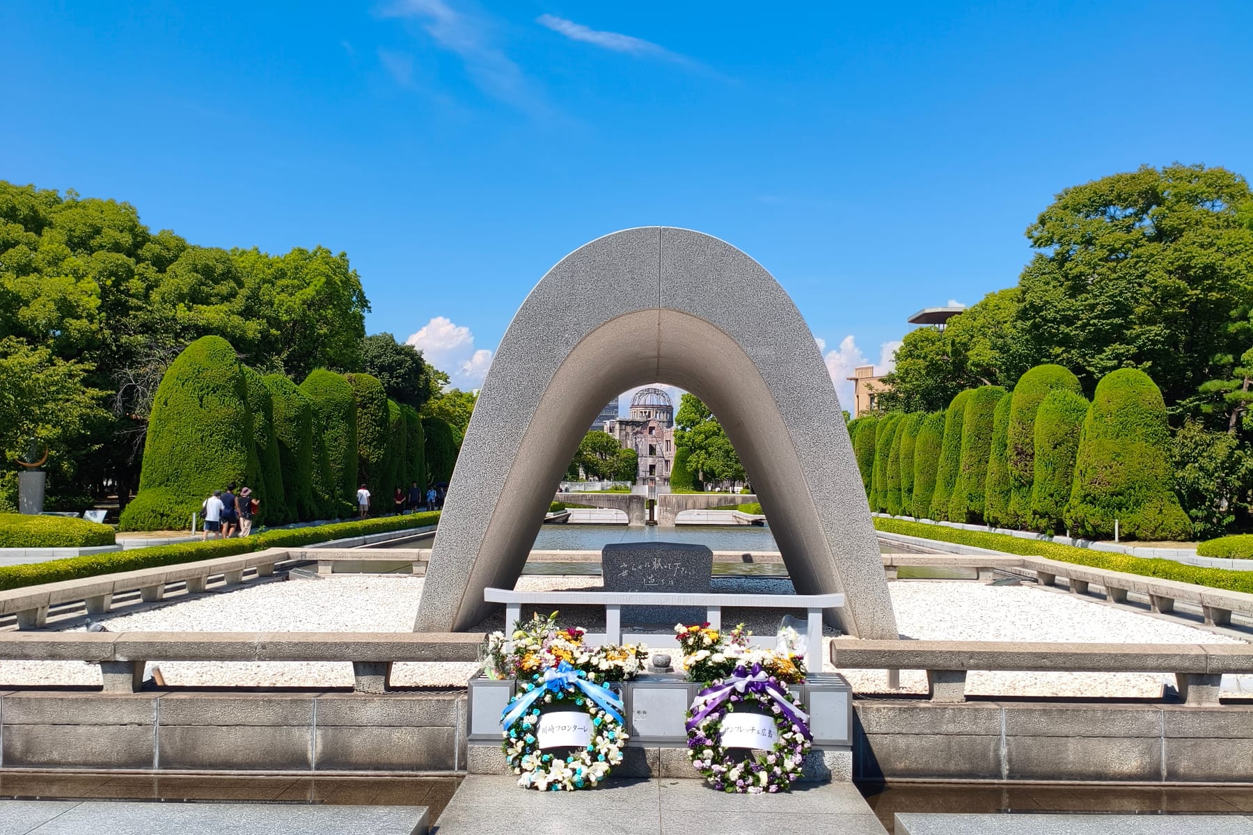 The Hiroshima Peace Memorial cenotaph arch with wreaths, framing the flame beyond